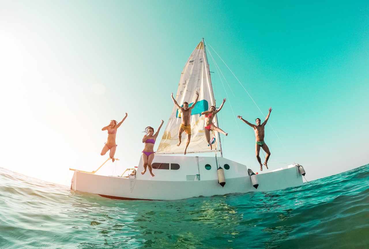 Happy crazy friends diving from sailing boat into the sea - Young people jumping inside ocean in summer vacation - Main focus on center guys - Travel and fun concept - Fisheye lens distortion